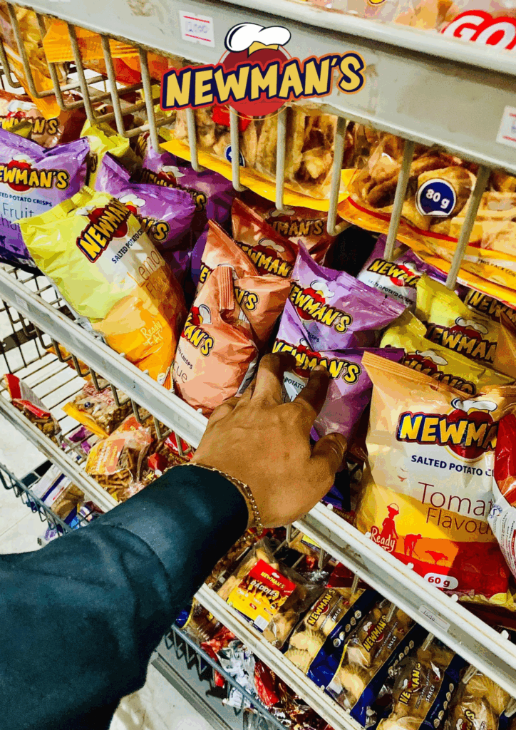 Hand reaching for a bag of Newman's branded Flavored Crisps on a brightly stocked supermarket shelf displaying various snack flavors.