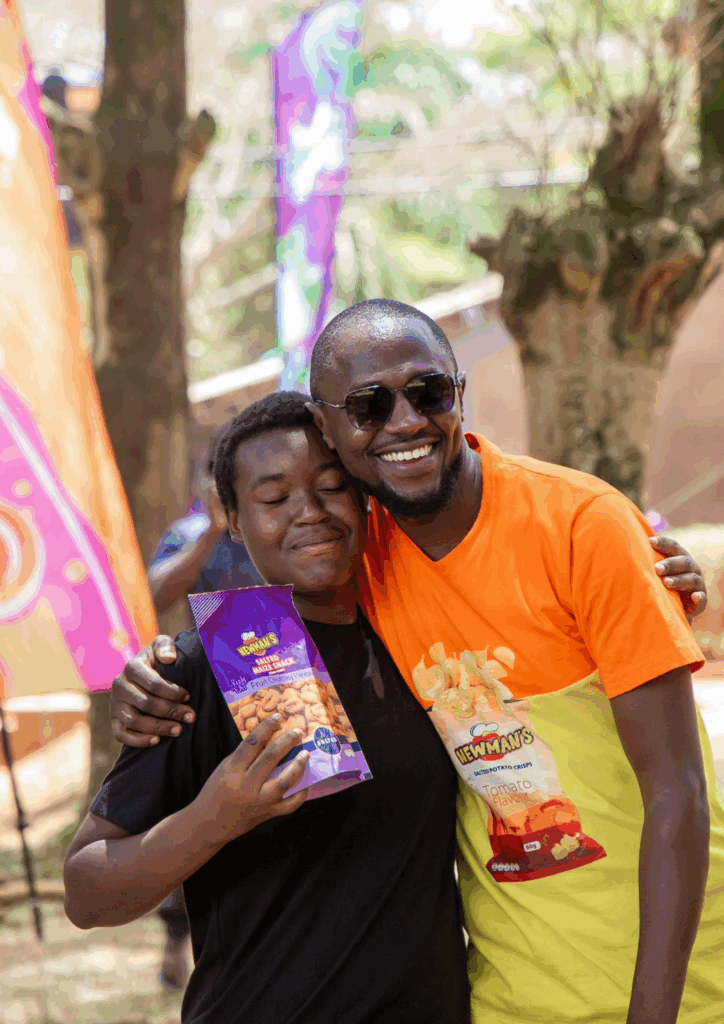 Two happy people hugging, one holding a bag of Newman's Maize Crisps, and the other wearing a shirt with Newman's Tomato Potato Crisps branding.