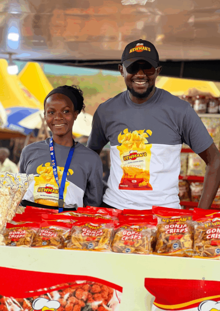 Two smiling Newman's employees behind a display of Gonja Crisps, highlighting the success of the 'Made in Uganda' brand.