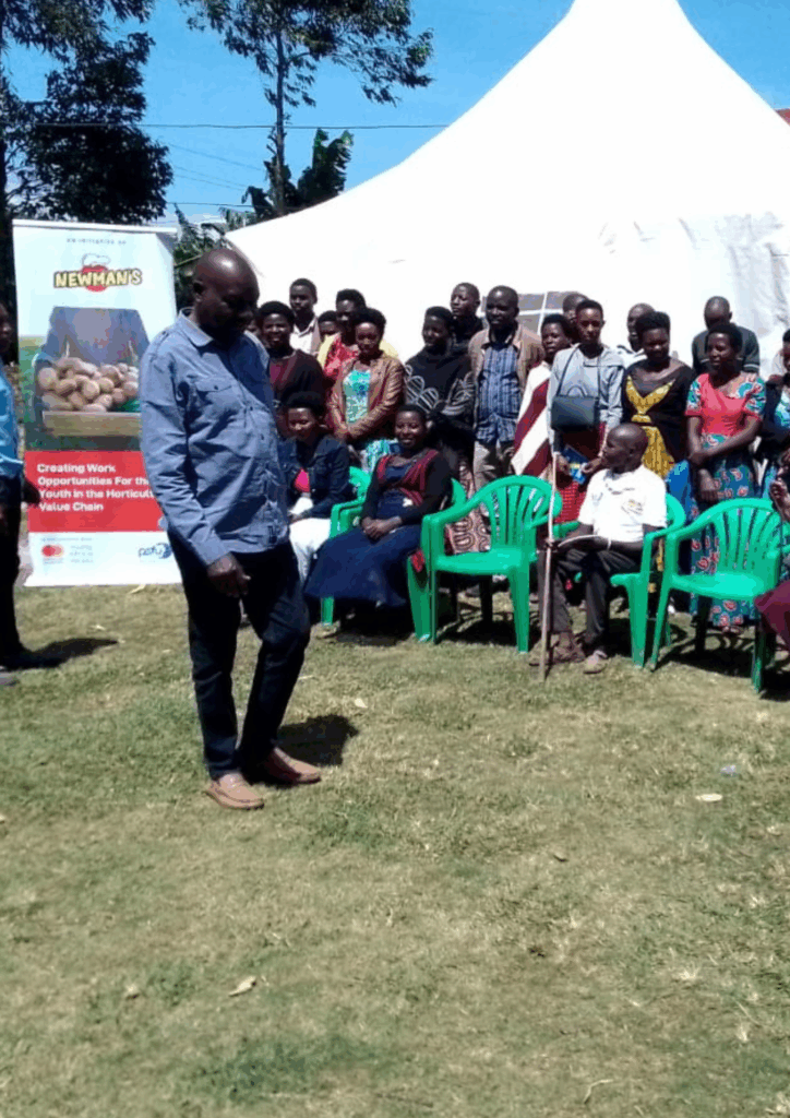 Group of farmers and community members seated in green chairs under a tent, listening to an instructor during a Newman's training session on the horticulture value chain.