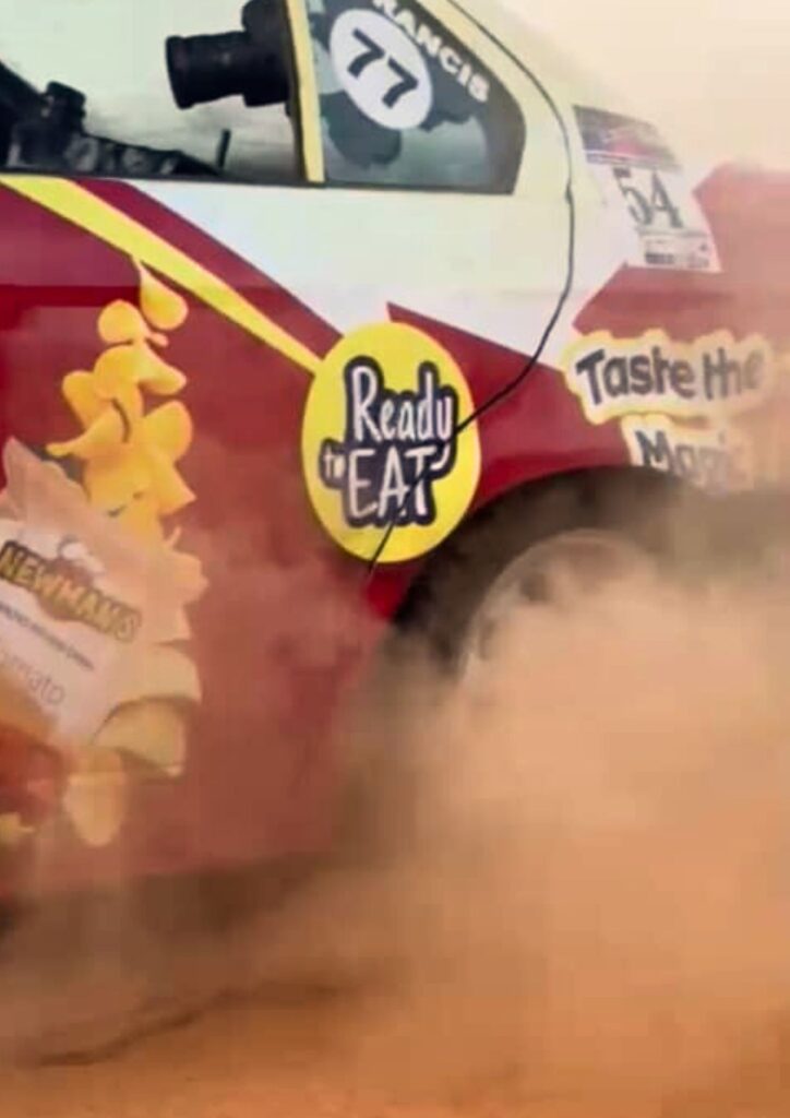 Rally car kicking up a cloud of red dust on the track, clearly showing Newman’s branding on the side