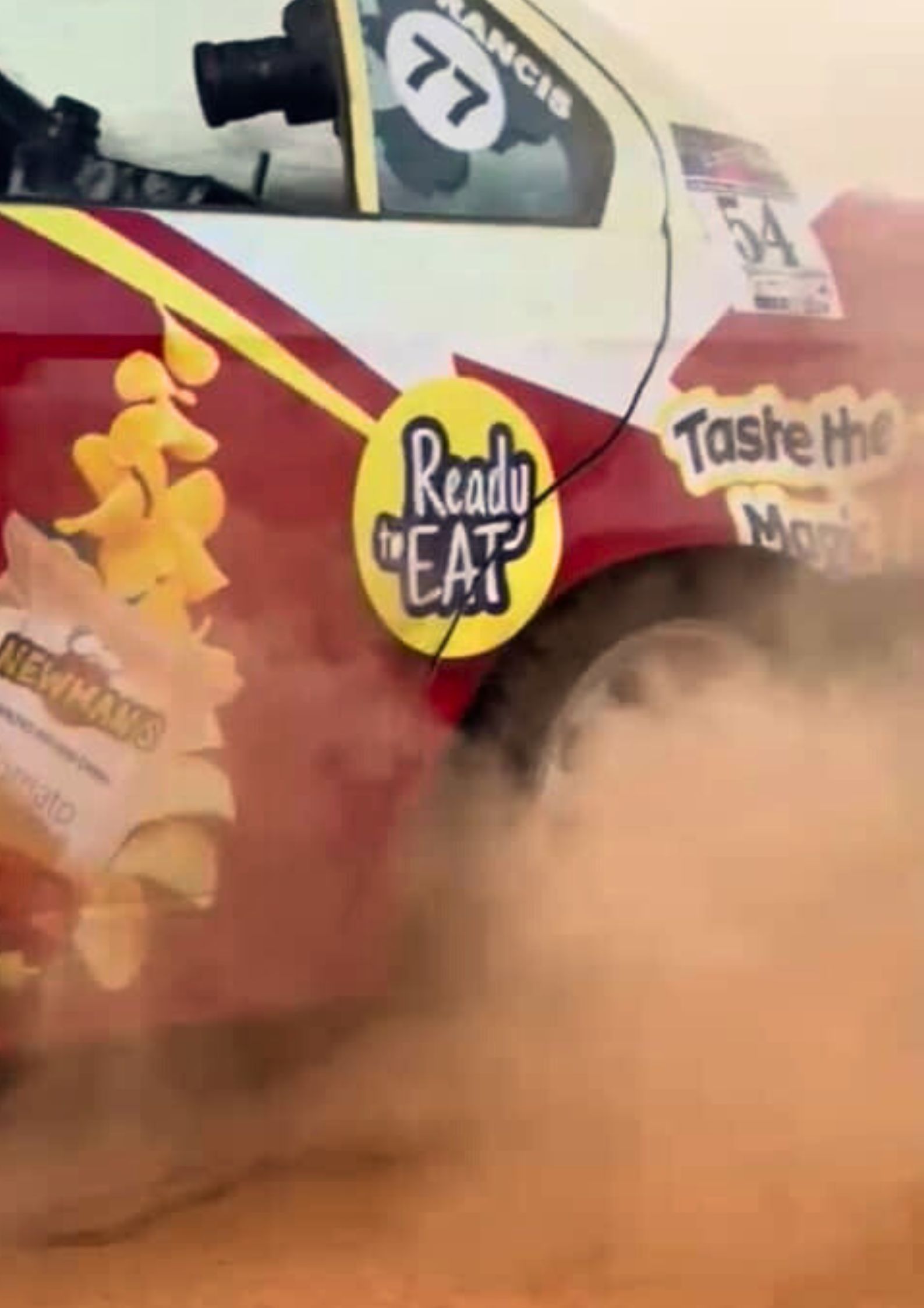 Rally car kicking up a cloud of red dust on the track, clearly showing Newman’s branding on the side