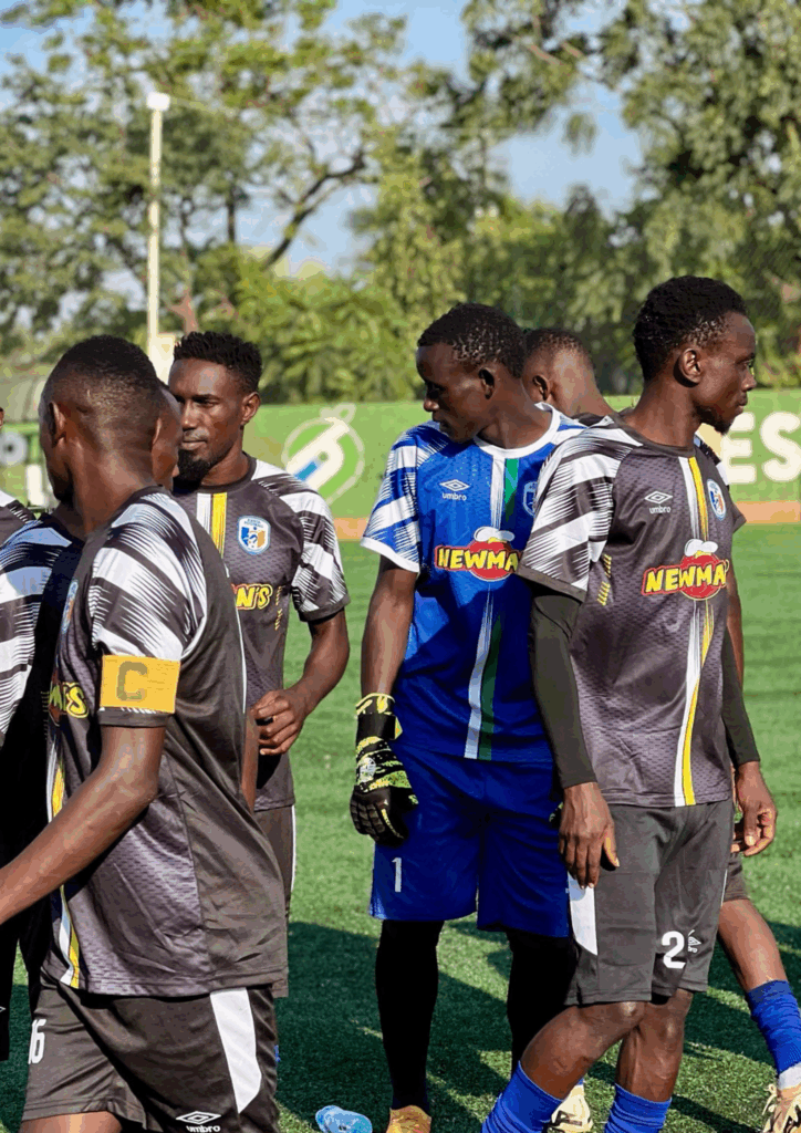The Newman's sponsored football team huddling on the pitch during the Kanta Football Tournament, wearing black, white, and yellow striped jerseys.