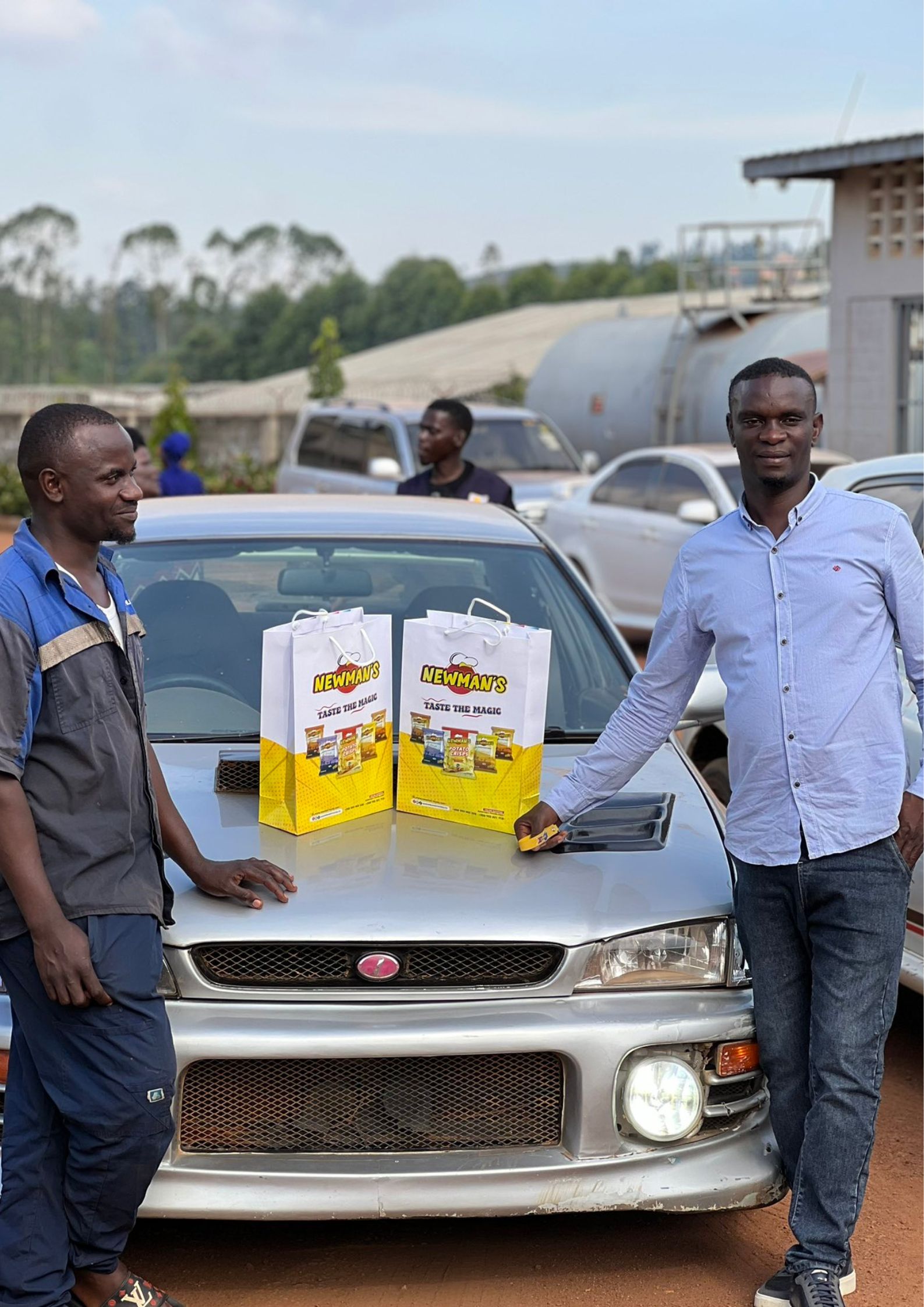 Two drivers standing next to a Subaru with Newman's bags of goodness on the car